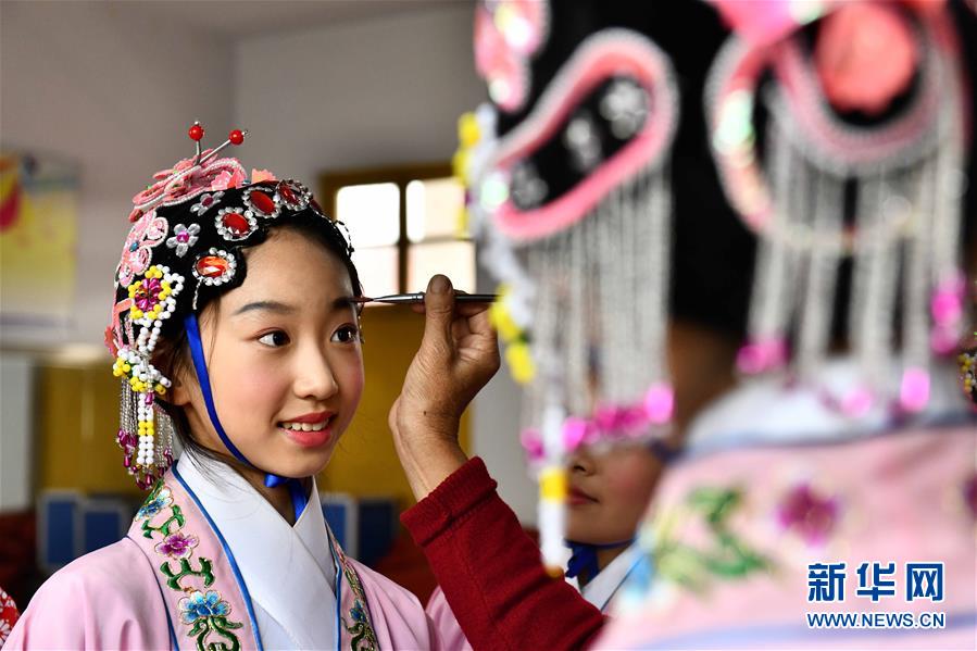 10月28日，在棗莊市臺兒莊區(qū)西關(guān)小學(xué)，文藝志愿者給小學(xué)員描眉。為傳承中華優(yōu)秀傳統(tǒng)文化，近年來山東省棗莊市臺兒莊區(qū)依托新時代文明實(shí)踐中心三級網(wǎng)絡(luò)，組織文藝志愿者作為校外輔導(dǎo)員，推動京劇、豫劇、柳琴戲、黃梅戲等優(yōu)秀傳統(tǒng)戲劇進(jìn)校園，讓小學(xué)員們體驗戲曲文化魅力。新華社記者 郭緒雷 攝