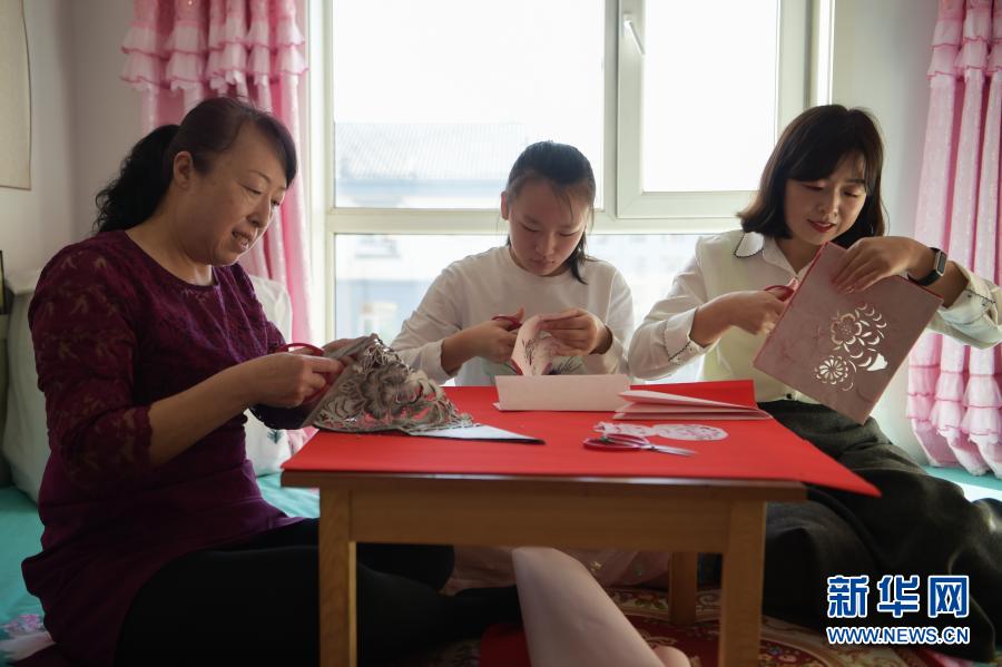 　　2月21日，在烏海市海南區(qū)新橋花園，李華（左）與外孫女高宇晨（中）、大女兒譚紅葉一起在家中剪紙。新華社記者 李志鵬 攝