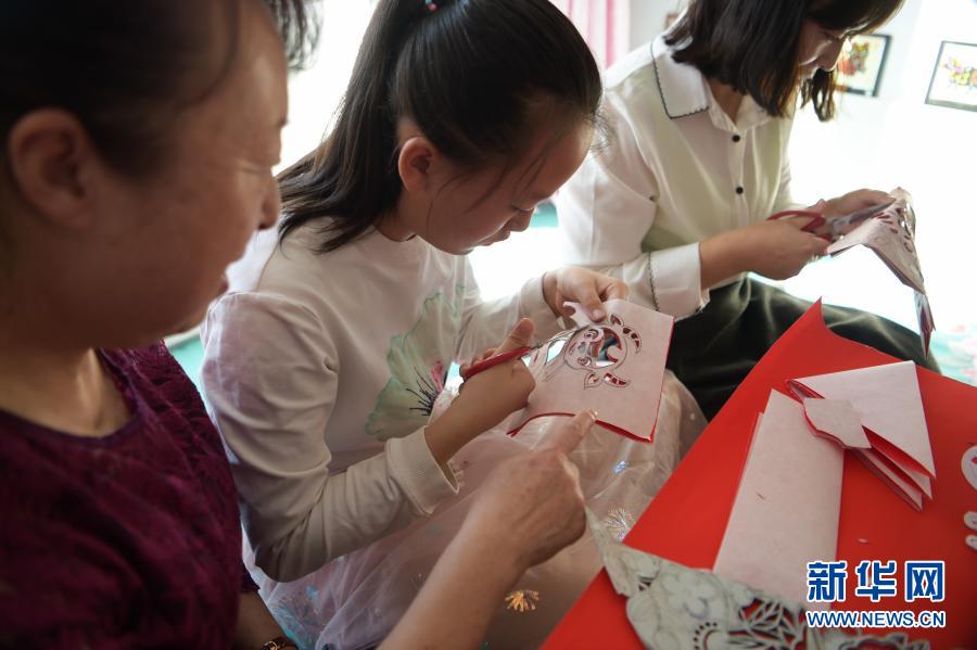　　2月21日，在烏海市海南區(qū)新橋花園，李華（左）在家中指導(dǎo)外孫女高宇晨（中）剪紙。新華社記者 李志鵬 攝